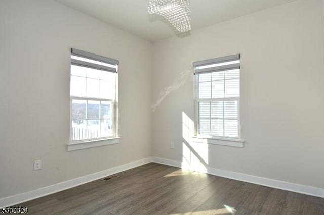 empty room with dark hardwood / wood-style flooring, plenty of natural light, and a notable chandelier