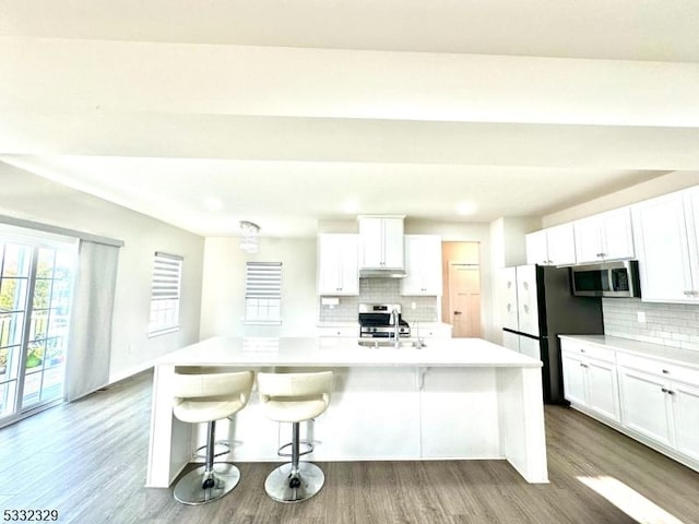 kitchen featuring white cabinets, appliances with stainless steel finishes, a kitchen island with sink, and a breakfast bar