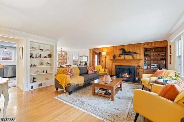 living room with light hardwood / wood-style flooring, an inviting chandelier, a wealth of natural light, and built in shelves