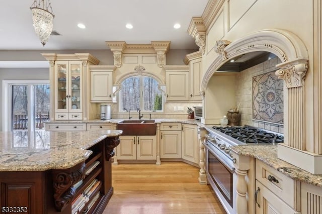 kitchen with hanging light fixtures, high end stove, decorative backsplash, sink, and cream cabinets