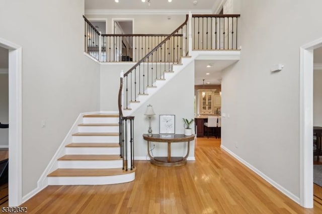 stairs with a high ceiling, hardwood / wood-style flooring, and ornamental molding