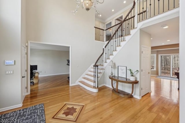 staircase with a towering ceiling, an inviting chandelier, crown molding, and wood-type flooring