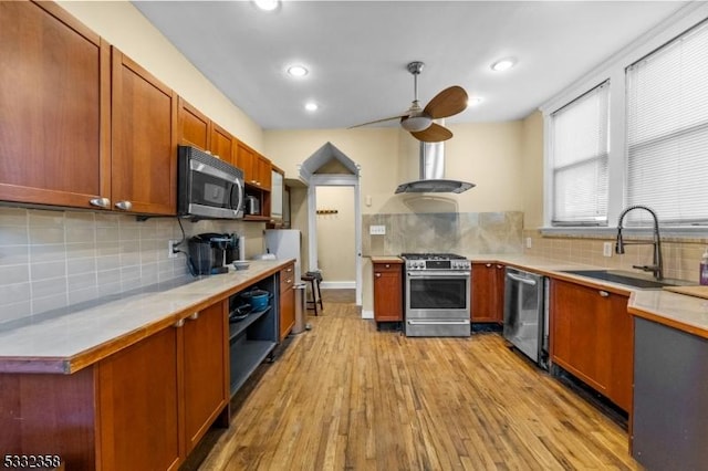 kitchen featuring ceiling fan, wall chimney range hood, sink, light wood-type flooring, and appliances with stainless steel finishes