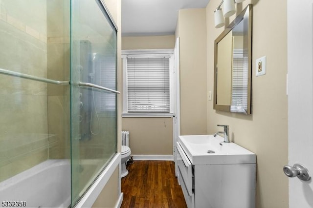 full bathroom featuring toilet, hardwood / wood-style flooring, bath / shower combo with glass door, vanity, and radiator heating unit