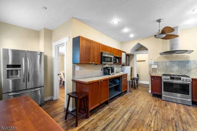 kitchen featuring tasteful backsplash, ceiling fan, island exhaust hood, appliances with stainless steel finishes, and dark hardwood / wood-style flooring