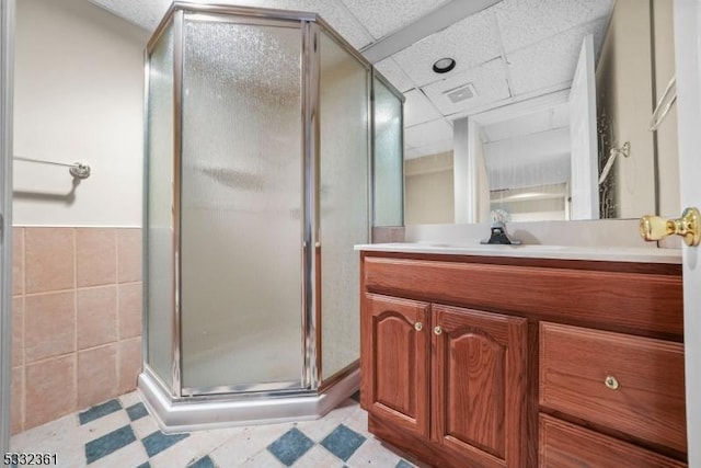 bathroom featuring tile walls, walk in shower, vanity, and a drop ceiling