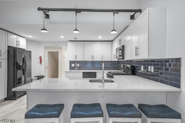 kitchen featuring black appliances, kitchen peninsula, sink, white cabinetry, and decorative light fixtures