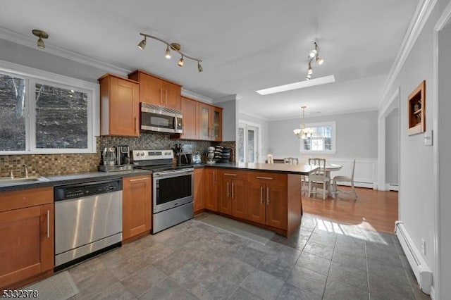 kitchen with kitchen peninsula, baseboard heating, pendant lighting, crown molding, and appliances with stainless steel finishes