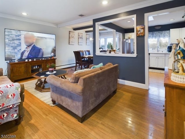 living room with a baseboard heating unit, sink, crown molding, and light hardwood / wood-style flooring