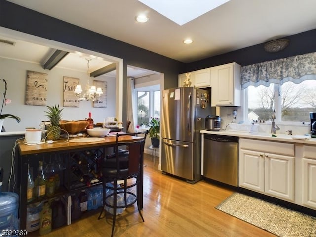 kitchen featuring light hardwood / wood-style flooring, beamed ceiling, decorative light fixtures, white cabinets, and appliances with stainless steel finishes