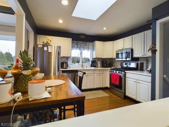 kitchen with dark wood-type flooring, sink, a skylight, appliances with stainless steel finishes, and white cabinetry