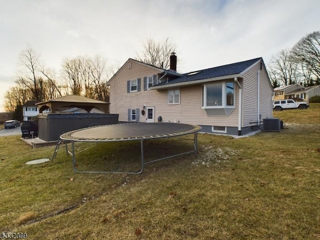 rear view of house featuring a trampoline, central AC unit, and a lawn