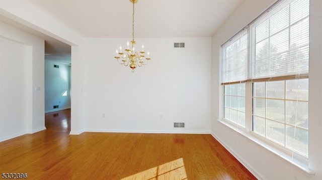 empty room with wood-type flooring and a chandelier