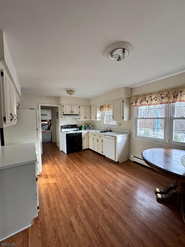 kitchen with white appliances, baseboard heating, sink, hardwood / wood-style floors, and white cabinetry