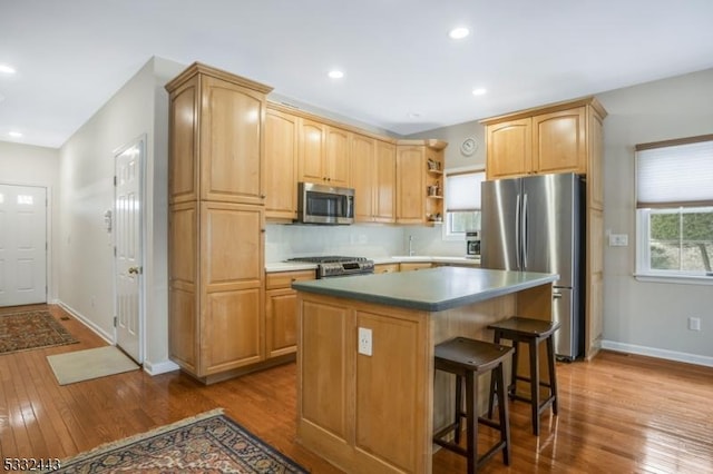 kitchen featuring a kitchen island, a kitchen bar, wood-type flooring, stainless steel appliances, and light brown cabinetry