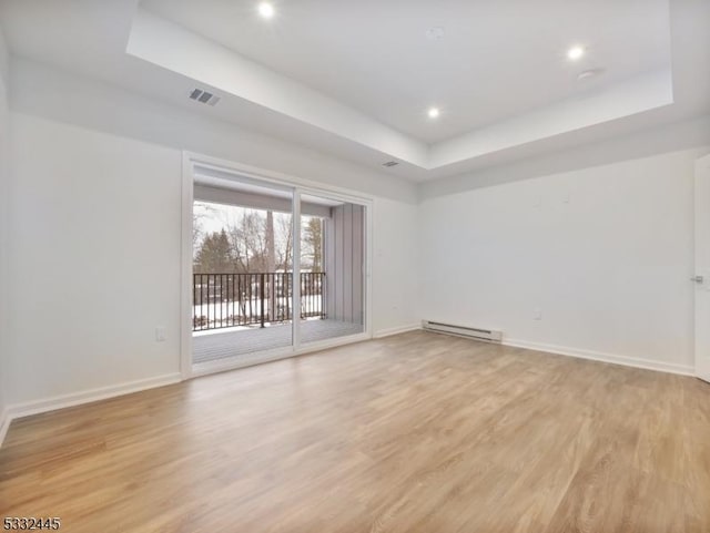 unfurnished room featuring a tray ceiling, a baseboard heating unit, and light hardwood / wood-style floors