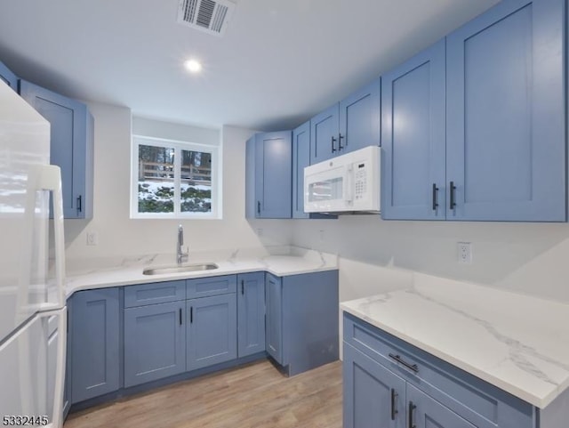 kitchen featuring blue cabinetry, light stone countertops, sink, white appliances, and light wood-type flooring