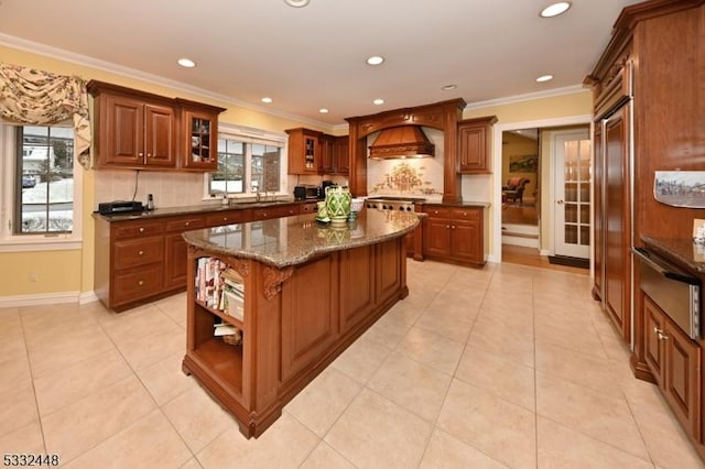 kitchen with a center island, backsplash, dark stone counters, ornamental molding, and custom range hood