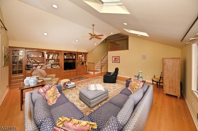 living room featuring built in shelves, ceiling fan, vaulted ceiling, and light wood-type flooring