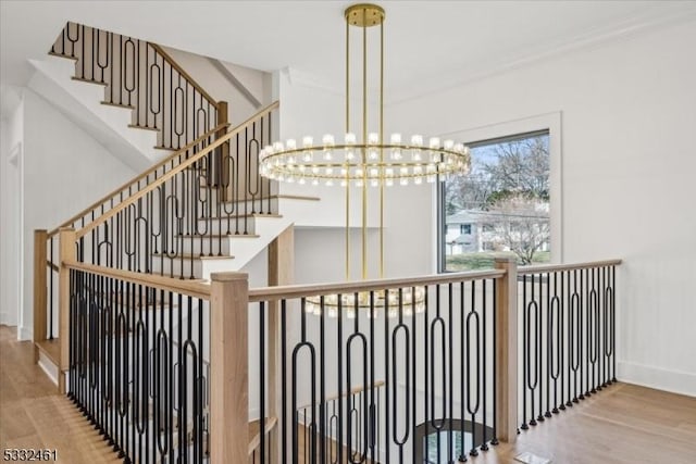 stairs featuring hardwood / wood-style flooring, crown molding, and an inviting chandelier