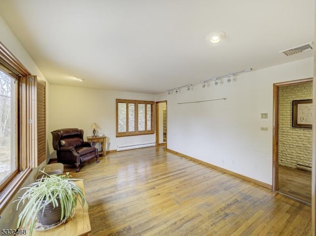 sitting room with rail lighting, visible vents, baseboard heating, and wood finished floors