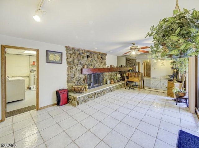 unfurnished living room featuring light tile patterned floors, ceiling fan, a stone fireplace, washer / clothes dryer, and rail lighting