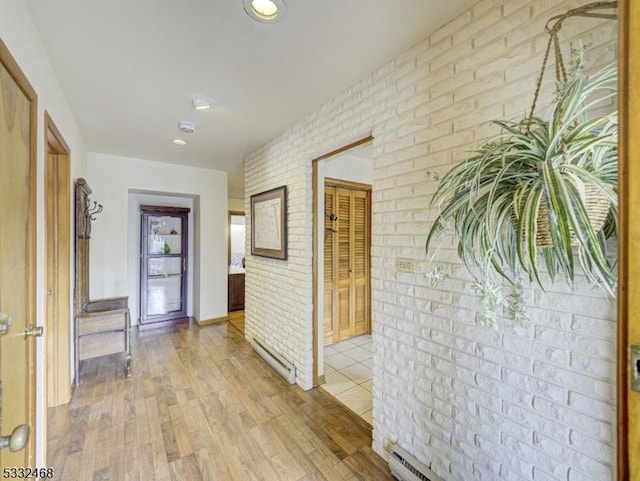 corridor with brick wall, light wood finished floors, and baseboard heating