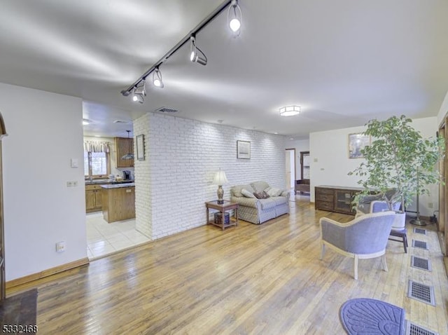 living room with brick wall, visible vents, and light wood-style floors