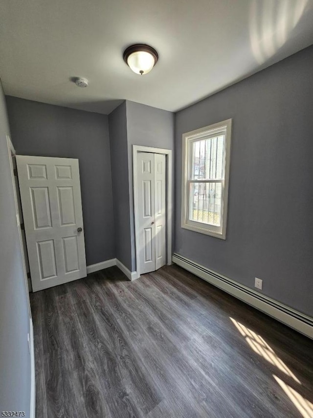 unfurnished bedroom with a baseboard radiator, a closet, and dark hardwood / wood-style floors