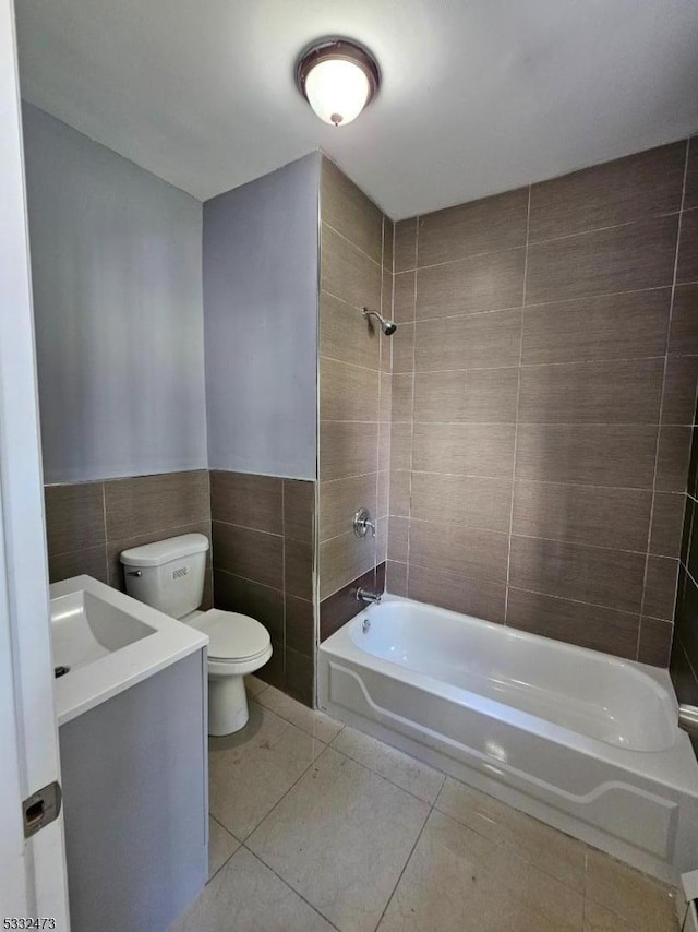 full bathroom featuring tiled shower / bath combo, tile patterned flooring, toilet, vanity, and tile walls