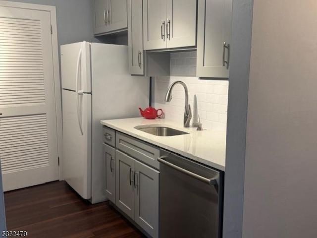 kitchen featuring gray cabinets, stainless steel dishwasher, decorative backsplash, sink, and dark wood-type flooring