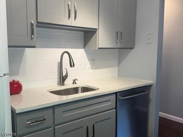 kitchen featuring gray cabinetry, tasteful backsplash, dishwasher, light stone countertops, and sink