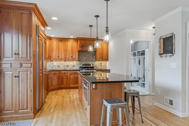 kitchen featuring stainless steel appliances, a kitchen island, ornamental molding, pendant lighting, and a breakfast bar