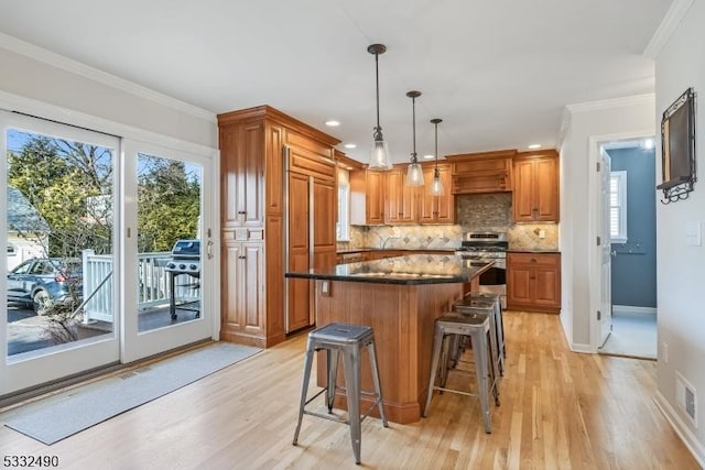 kitchen with tasteful backsplash, decorative light fixtures, light wood-type flooring, stainless steel stove, and a center island