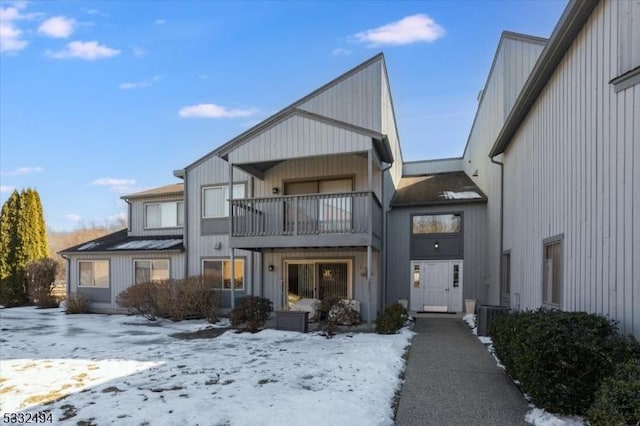 snow covered back of property featuring a balcony and central AC unit