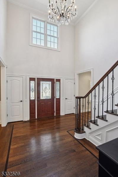 entryway with crown molding, stairway, a high ceiling, an inviting chandelier, and dark wood-type flooring