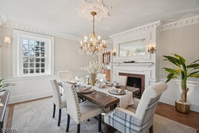 dining space with hardwood / wood-style flooring, crown molding, a chandelier, and a brick fireplace