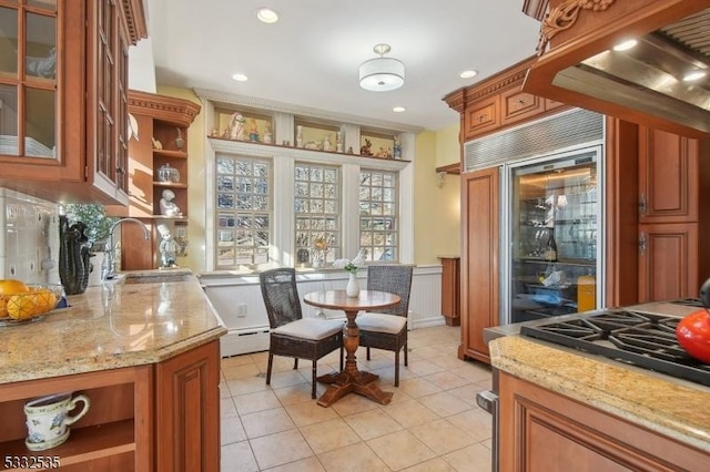 interior space featuring stainless steel built in refrigerator, sink, light tile patterned floors, baseboard heating, and light stone countertops