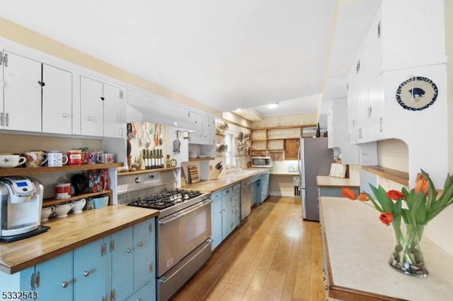 kitchen featuring butcher block countertops, white cabinetry, blue cabinetry, and appliances with stainless steel finishes