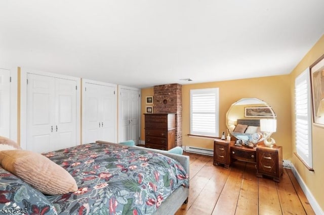 bedroom featuring multiple windows, wood-type flooring, baseboard heating, and two closets