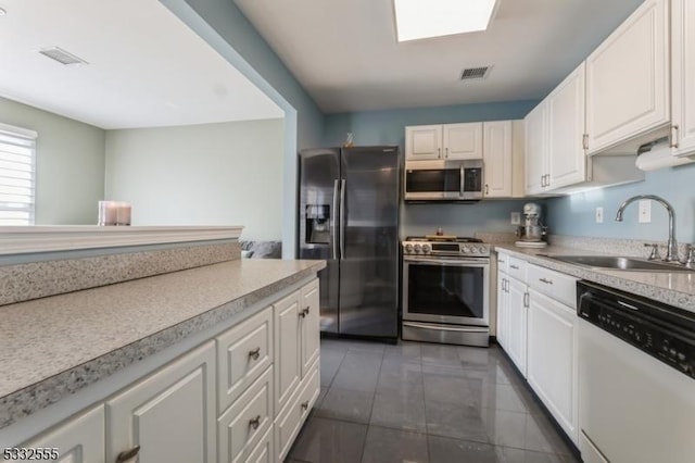 kitchen featuring sink, appliances with stainless steel finishes, a skylight, white cabinets, and dark tile patterned flooring