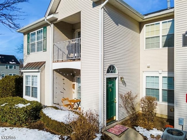 snow covered property entrance with central AC and a balcony