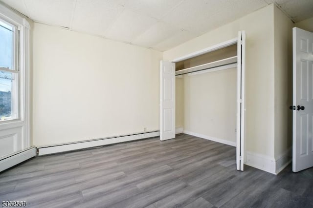 unfurnished bedroom with baseboard heating, a closet, and hardwood / wood-style flooring