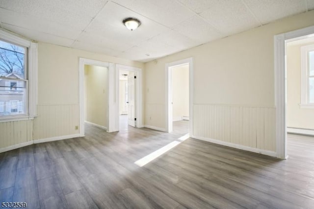 empty room with a drop ceiling, wood-type flooring, radiator heating unit, and baseboard heating