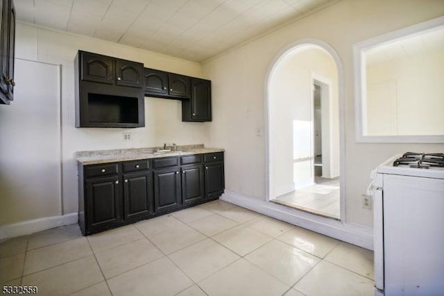 kitchen featuring light tile patterned floors, ornamental molding, gas range gas stove, and sink