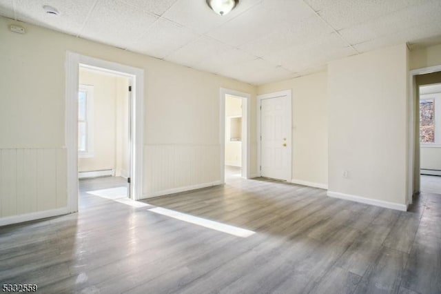 spare room with hardwood / wood-style floors, a drop ceiling, and a baseboard heating unit