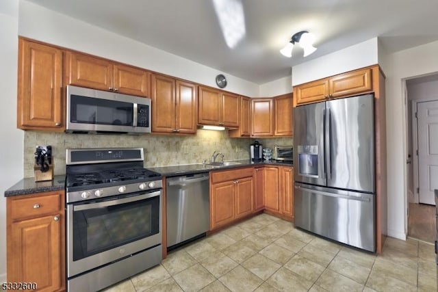 kitchen with decorative backsplash, light tile patterned flooring, sink, appliances with stainless steel finishes, and dark stone counters