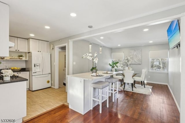 kitchen with dark wood-type flooring, backsplash, range hood, white refrigerator with ice dispenser, and white cabinets