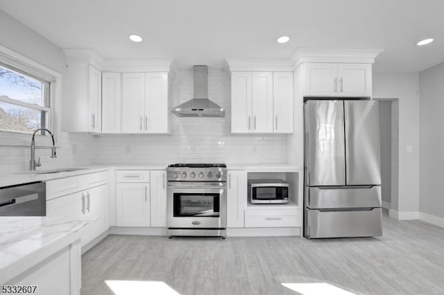 kitchen featuring tasteful backsplash, wall chimney range hood, stainless steel appliances, white cabinetry, and a sink