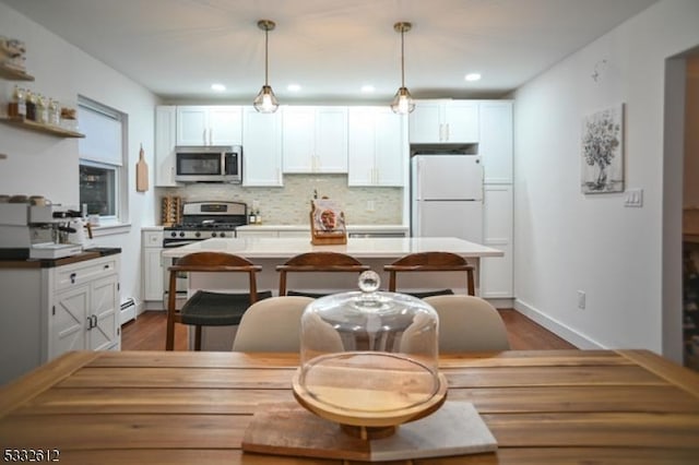 kitchen with stainless steel appliances, backsplash, pendant lighting, white cabinets, and hardwood / wood-style flooring